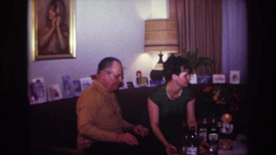 1967 Rockaway Beach frame of a woman leaning toward a low table as a seated man watches in a private living room.