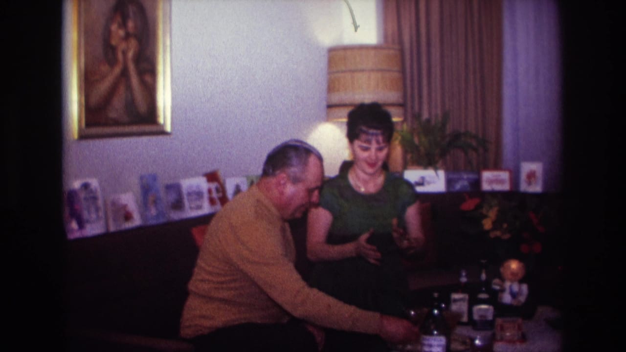 Seated couple reaches toward drinks on a table in a decorated living room.