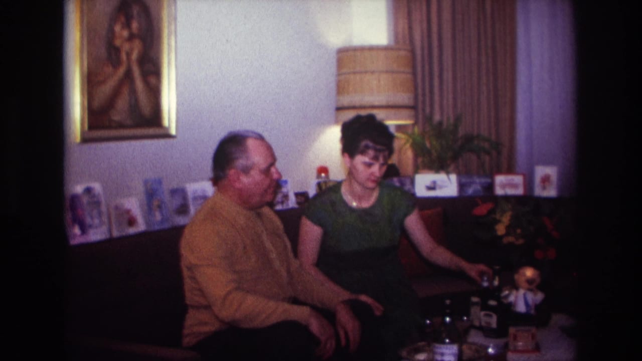 Man and woman sit side by side on a couch with table objects in front of them.