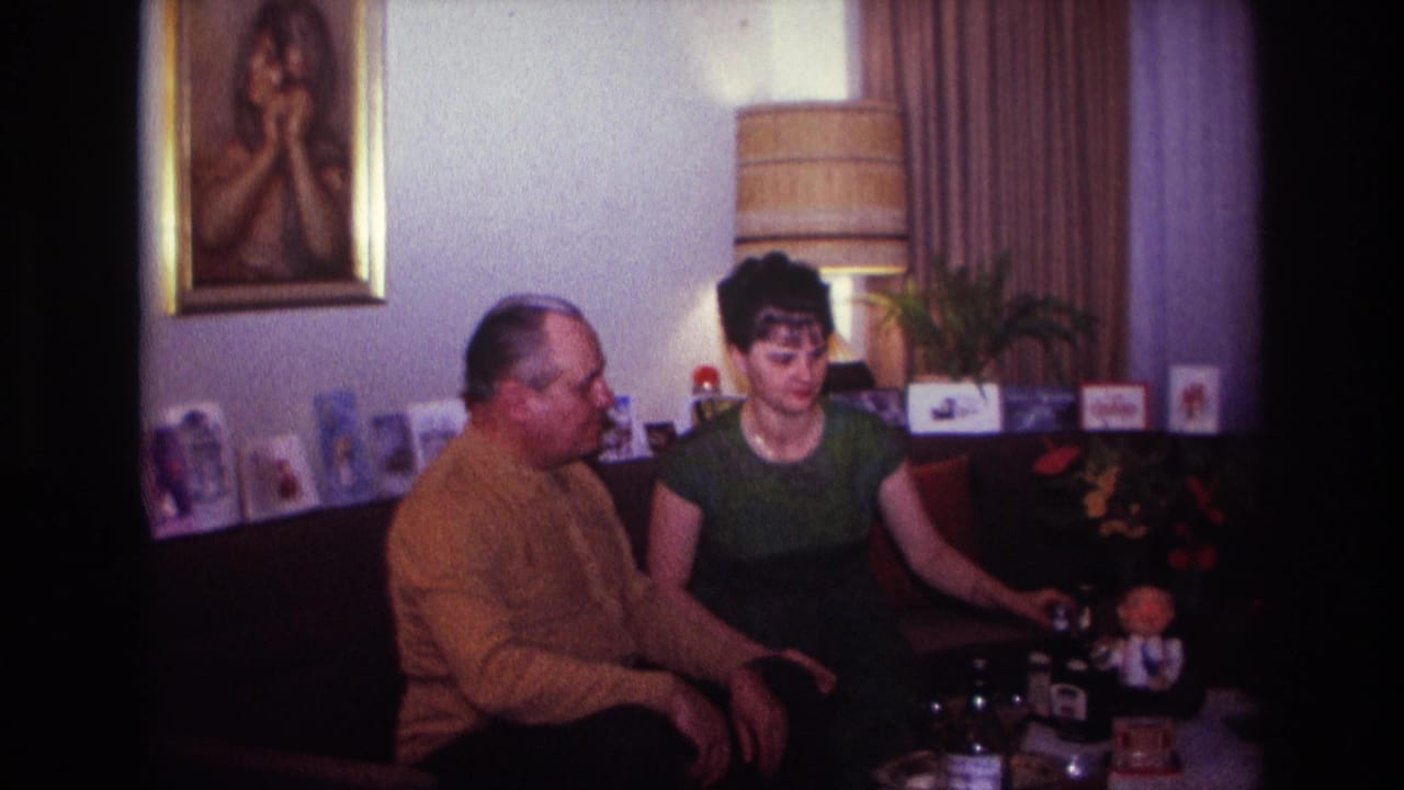 1967 Rockaway Beach home-movie frame of an adult couple seated together in a decorated living room interior.