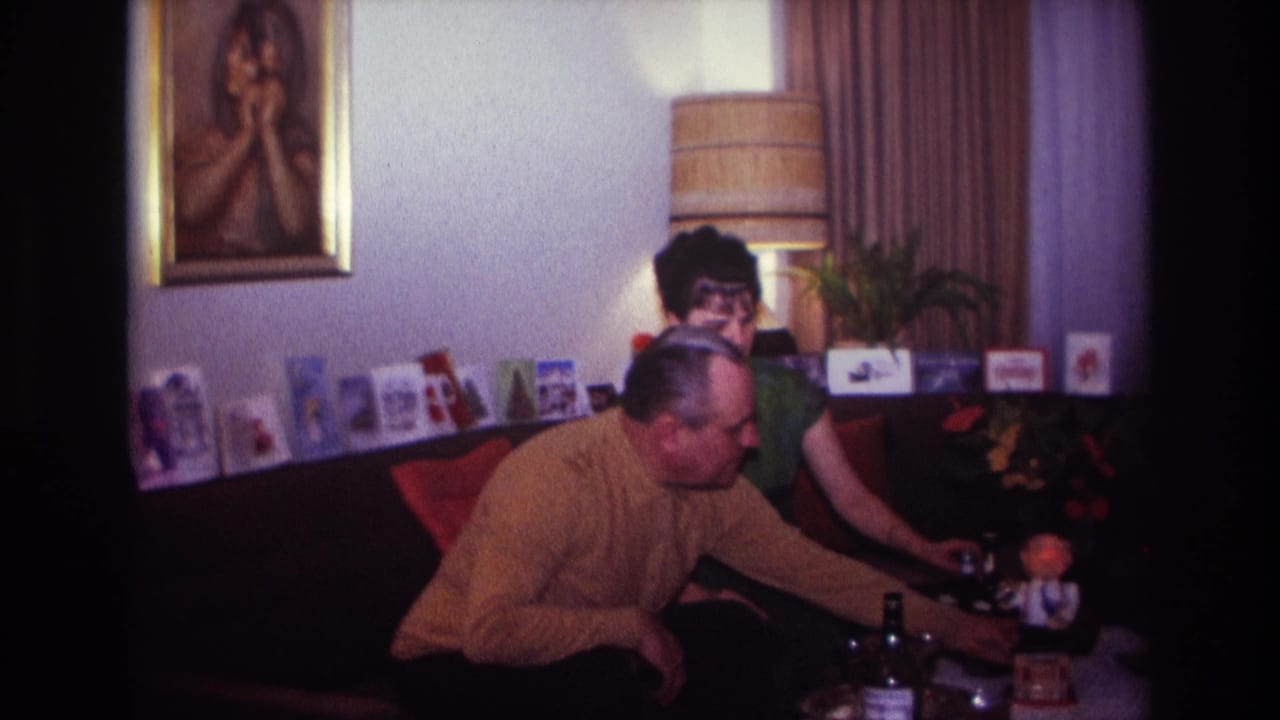 1967 Rockaway Beach home-movie frame showing the man reaching toward a low table as the woman remains seated beside him.