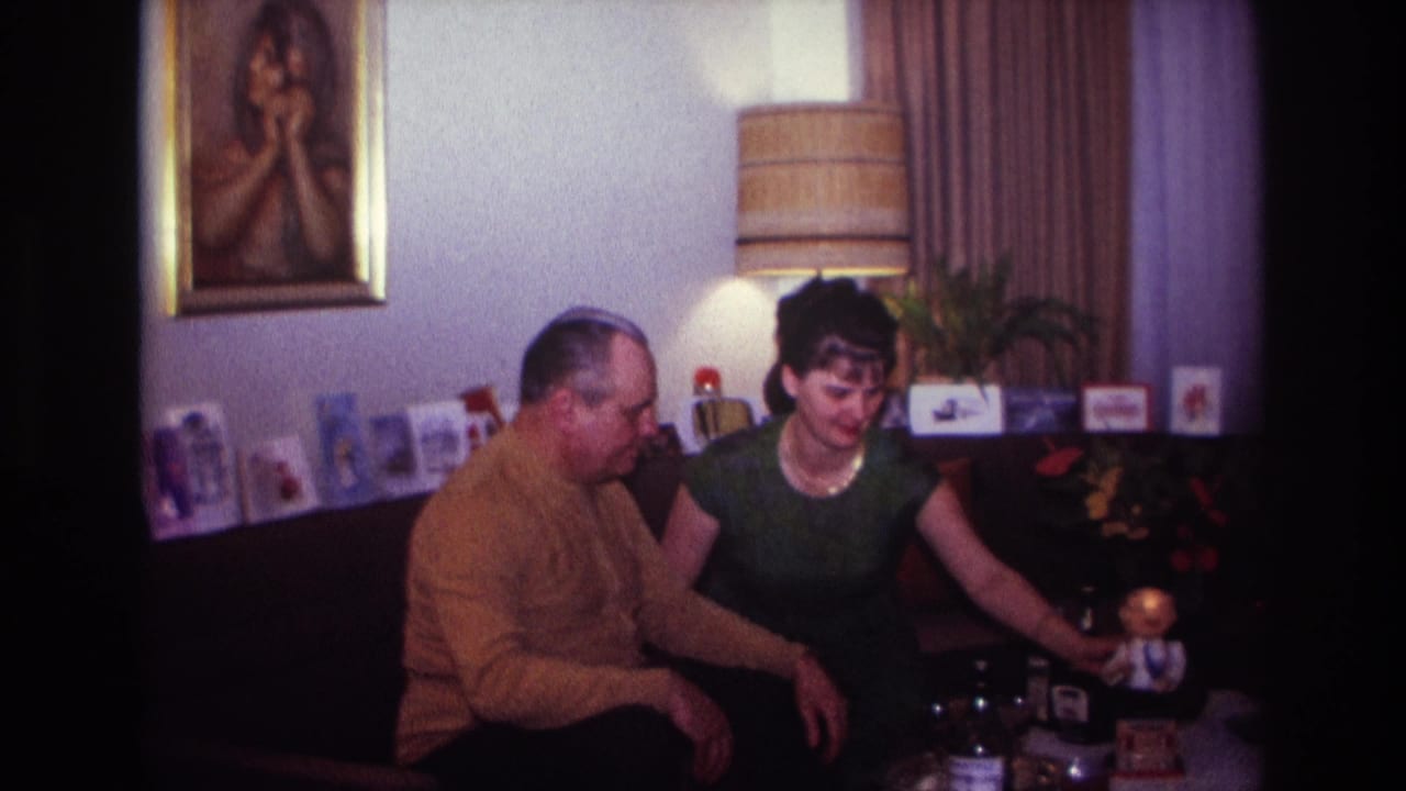 Man and woman seated beside a table with bottles, glasses, and a small toy figure.