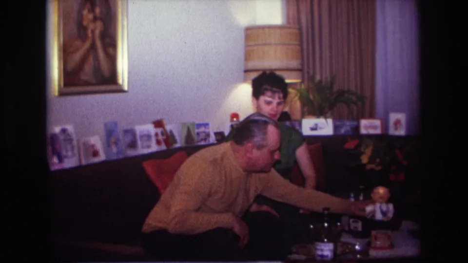1967 Rockaway Beach home interior with a man leaning toward a small toy as a woman looks down from behind the couch area.