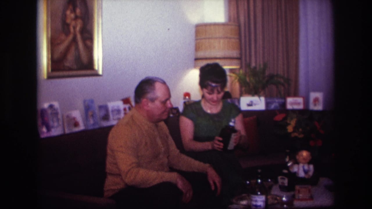 Woman seated on a couch holds a dark bottle while a man sits beside her.