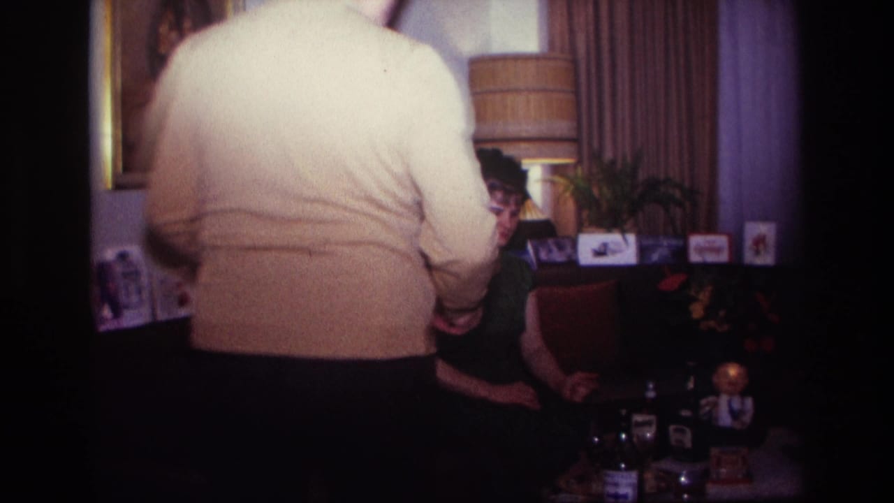 Man in a cream sweater stands in front of the seated woman, partly blocking the living room view.