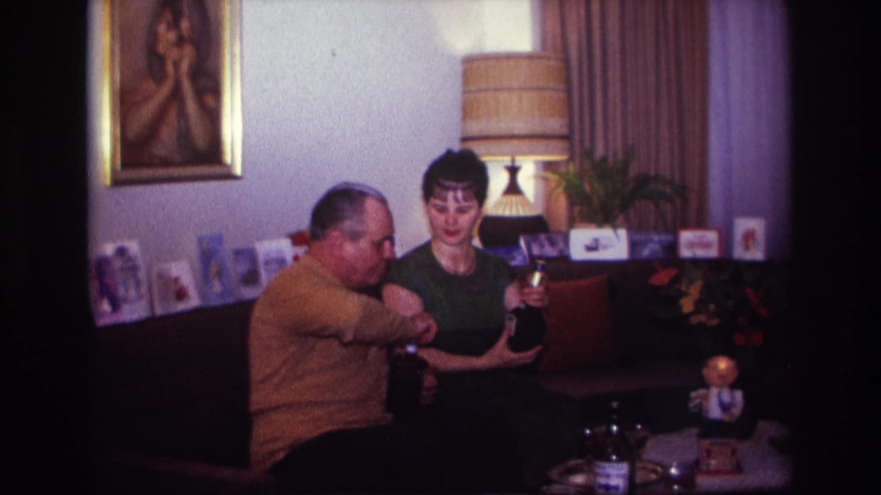 Man opens or adjusts a bottle while the woman holds a small glass and another bottle.