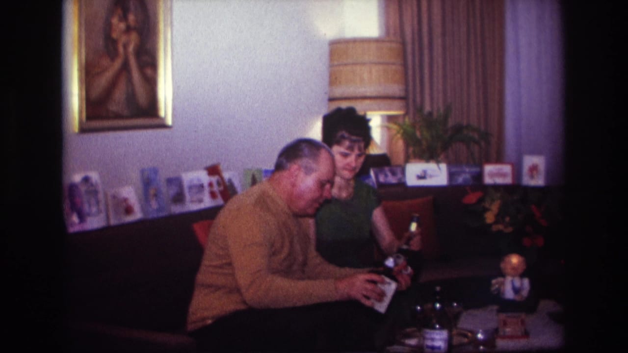 A man and woman sit on a couch as the man reaches toward items on a low table.