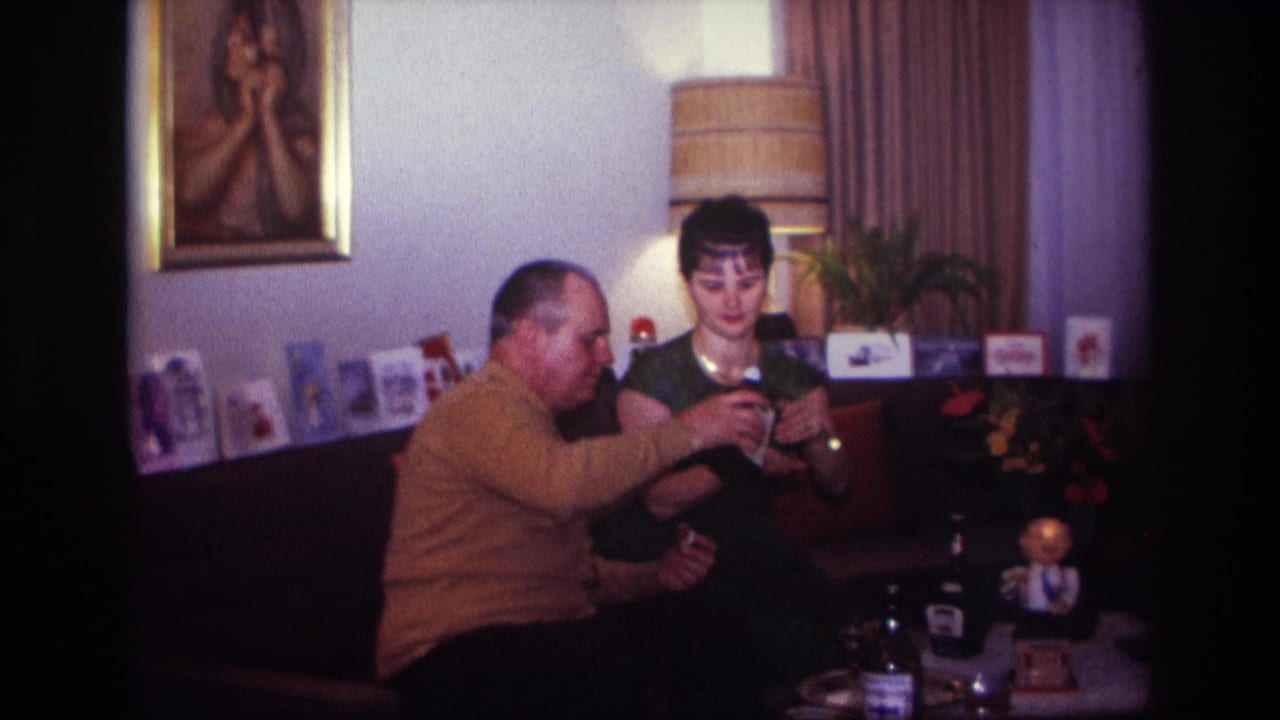 1967 Rockaway Beach home-movie frame of two adults on a couch as the man handles a liquor bottle and the woman holds a glass.