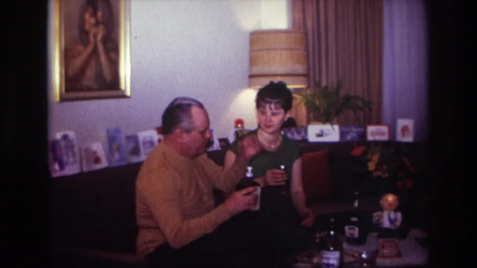 1967 Rockaway Beach home interior showing a woman with a glass and a man holding a bottle on a couch.