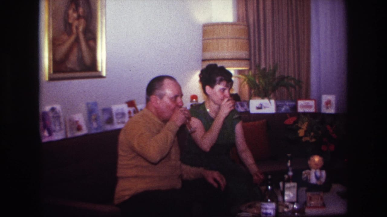 The man and woman sip their drinks in a Rockaway Beach living room, with a striped lamp and greeting cards behind them.