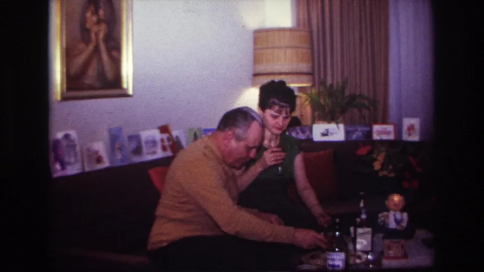The couple remain seated in the Rockaway Beach home interior as the man reaches toward the table and the woman holds her drink.