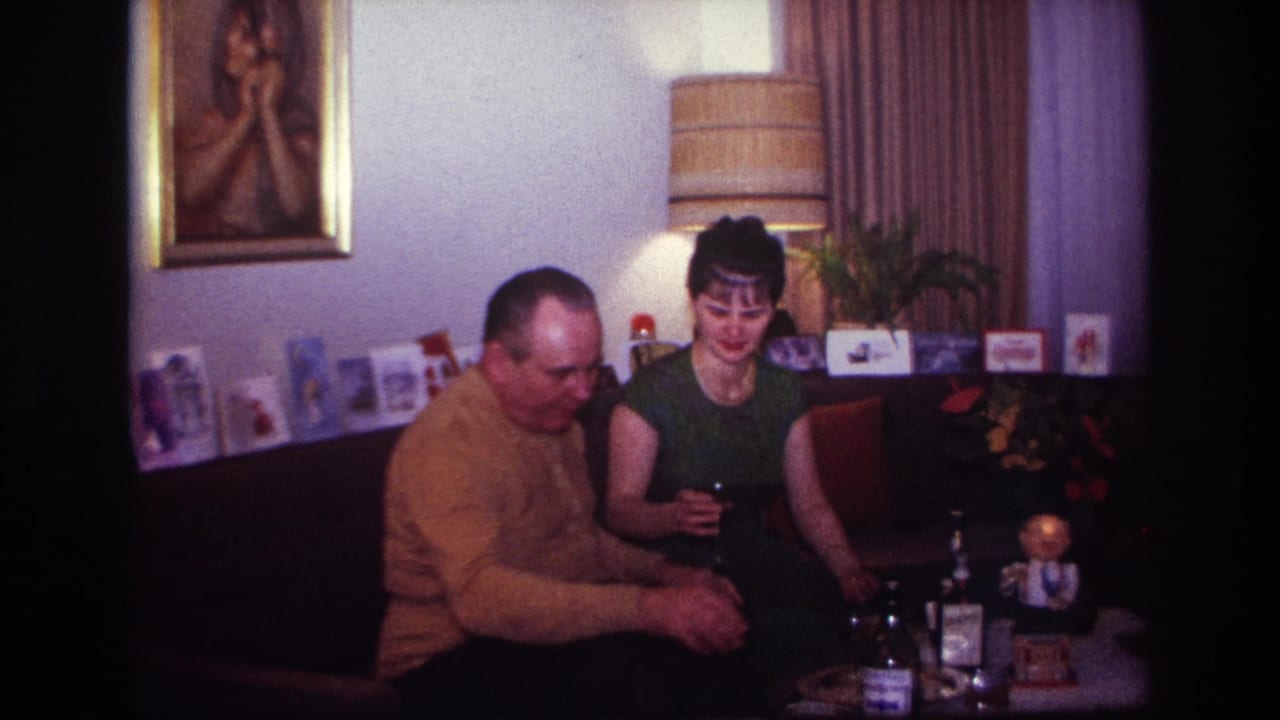 The couple sits close together as the woman holds a drink beside bottles and holiday cards.