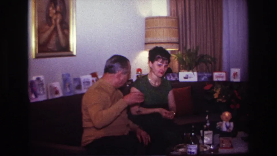 The couple continues their living-room exchange in Rockaway Beach, with drinks, cards, curtains and framed art visible.