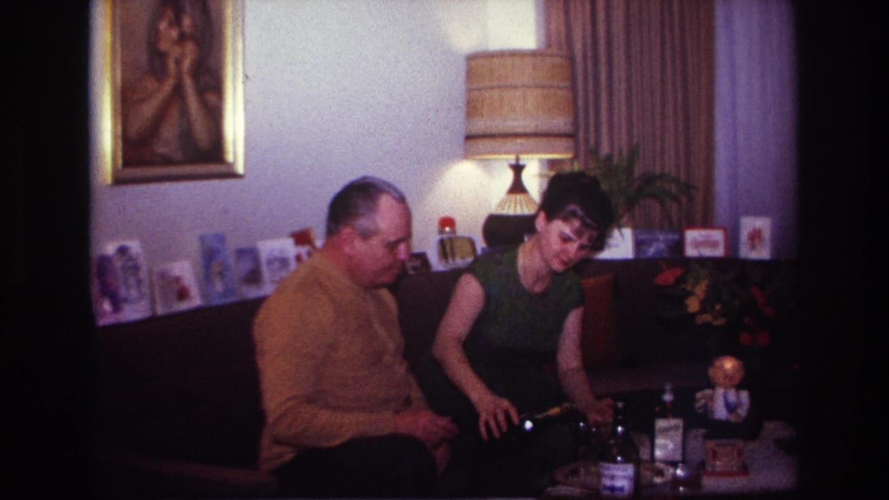 The woman leans forward toward bottles and glasses in the Rockaway Beach living room while the man remains seated beside her.