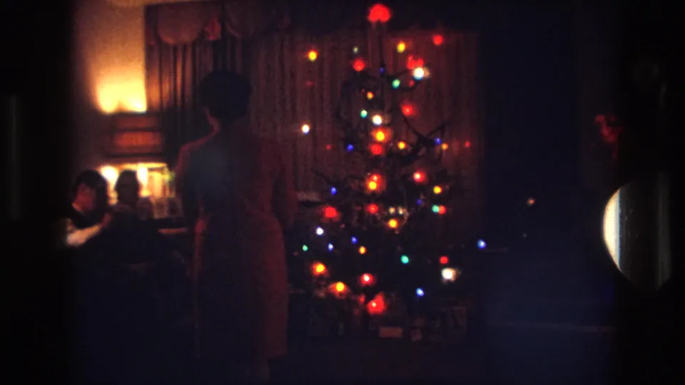 Out-of-focus 1967 Rockaway Beach holiday frame with a lit Christmas tree, warm lamp light and people in shadow nearby.