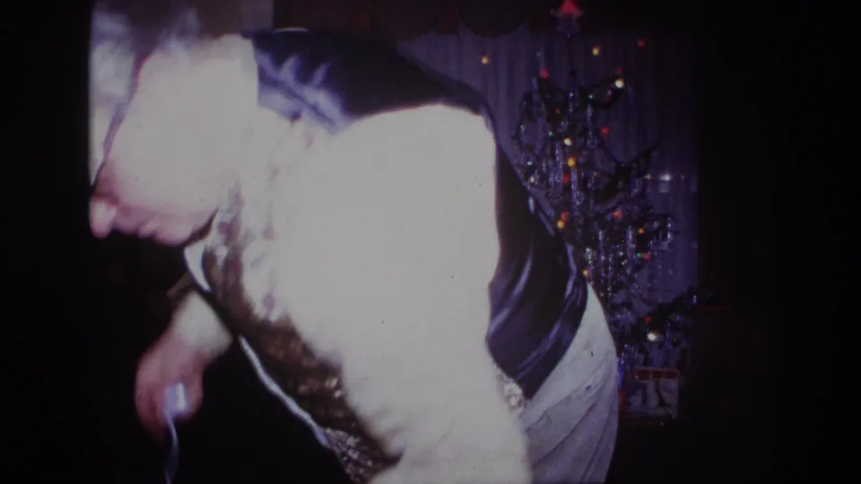 Close 8mm frame of the man in glasses and vest moving through a dim 1967 Rockaway Beach Christmas interior.