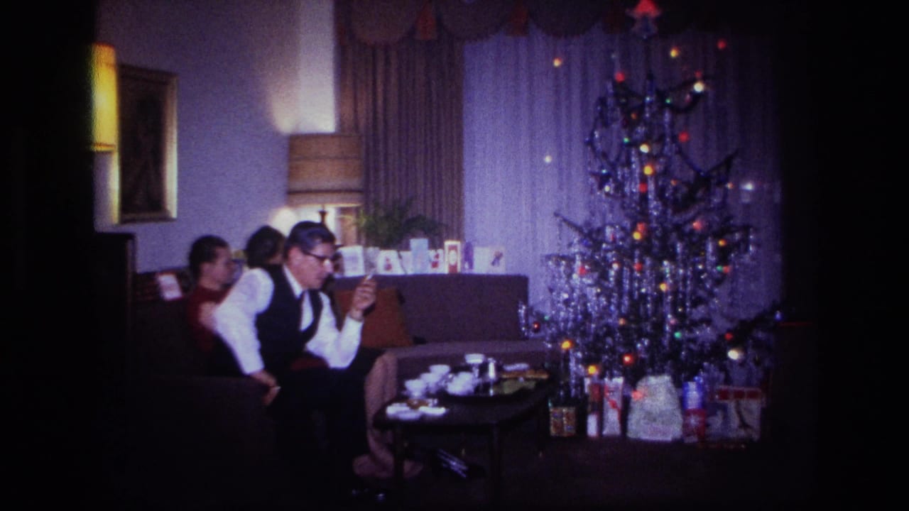 Adults sit on a sofa near a lit Christmas tree and coffee table.