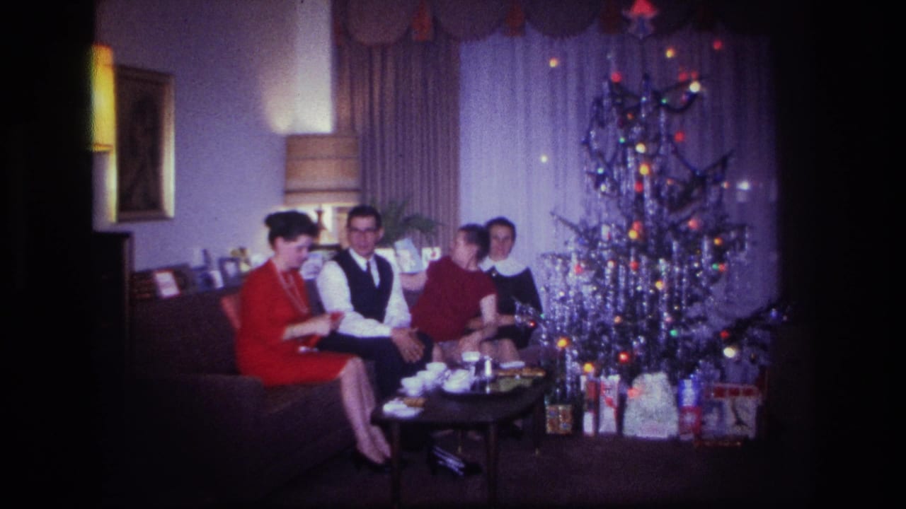 Adults sit together on a couch near a lit Christmas tree and coffee table.