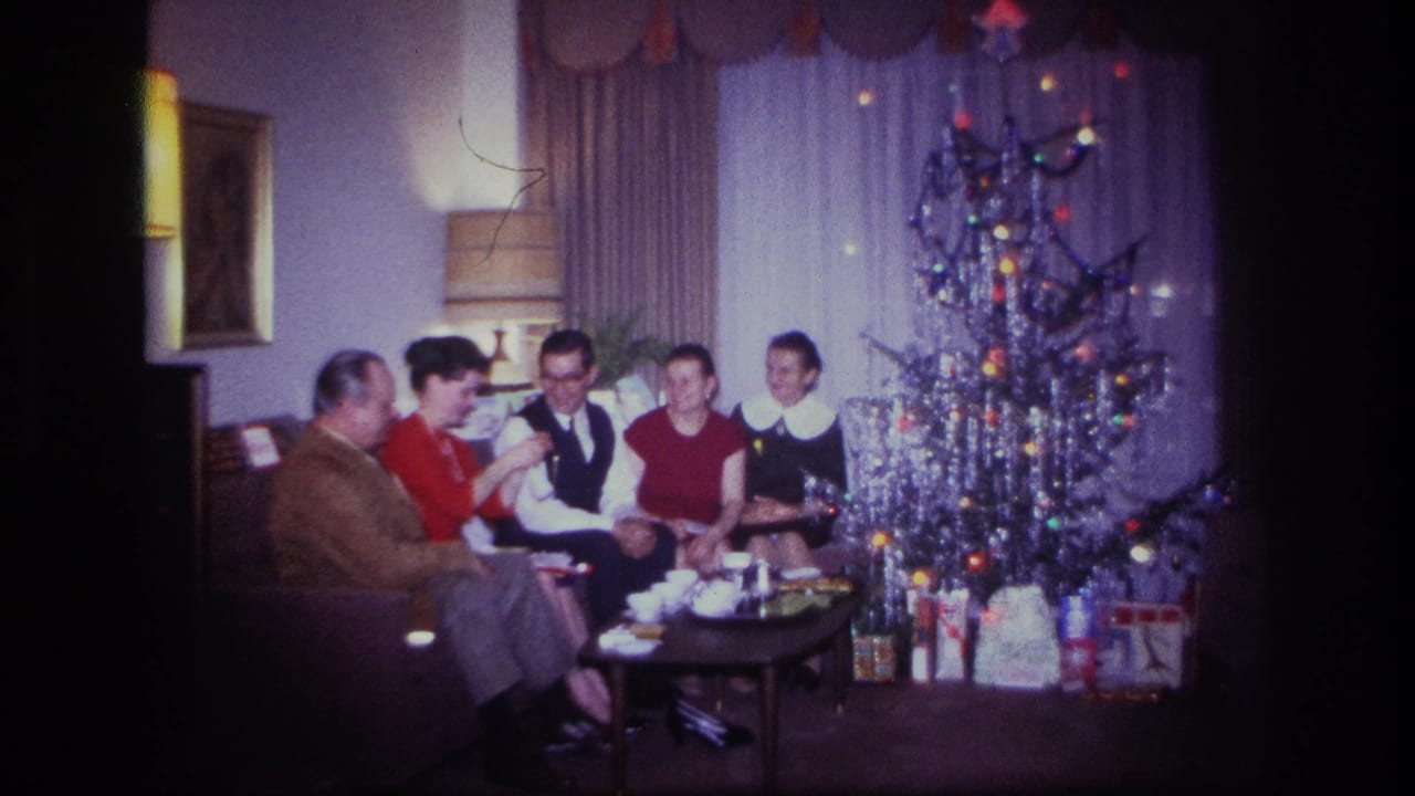 1967 Rockaway Beach home-movie frame showing five people on a sofa near a silver tinsel Christmas tree and wrapped presents.