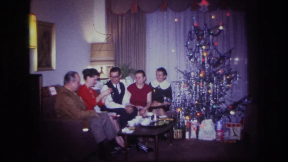 1967 Rockaway Beach home-movie frame showing five people on a sofa near a silver tinsel Christmas tree and wrapped presents.