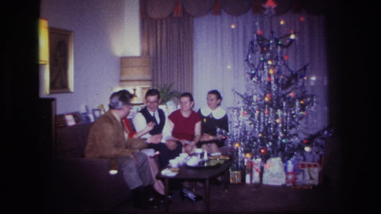 Seated group laughing and talking beside a decorated Christmas tree and presents.
