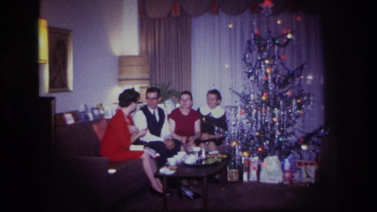 1967 Rockaway Beach home-movie frame showing a family seated near an aluminum Christmas tree and wrapped gifts in a private living room.