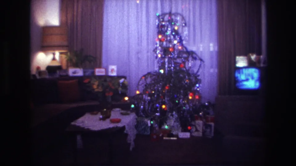 Rockaway Beach 1967 home-movie frame showing a decorated Christmas tree, wrapped presents, curtains, lamp, and small television indoors.