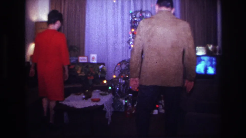 1967 Rockaway Beach home-movie frame with two adults walking toward a tinsel Christmas tree beside a small television.