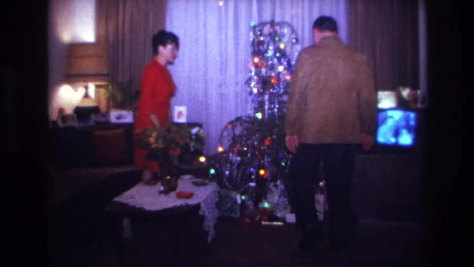 1967 Rockaway Beach holiday home-movie frame of adults beside a decorated tinsel tree, coffee table, lamps, and television.