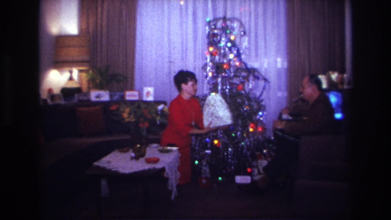 1967 Rockaway Beach living-room scene with a woman in red and a man beside a silver tinsel tree and large wrapped gift.