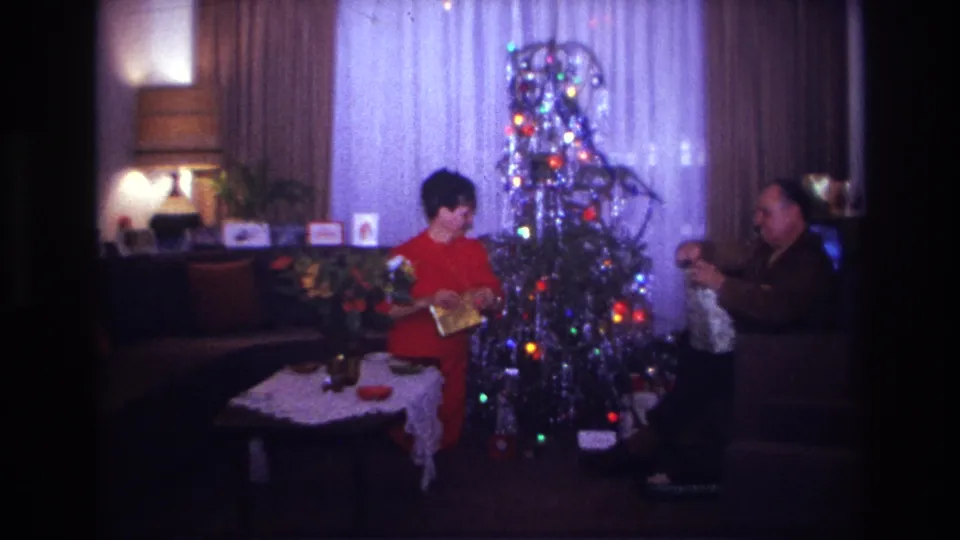 1967 Rockaway Beach Christmas frame showing the woman holding a newly opened present near a silver tinsel tree in a private living room.