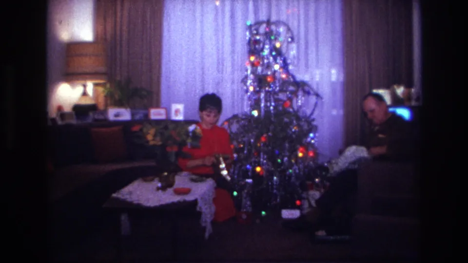 1967 Rockaway Beach frame showing two adults in a private living room with a lit aluminum Christmas tree and holiday items.