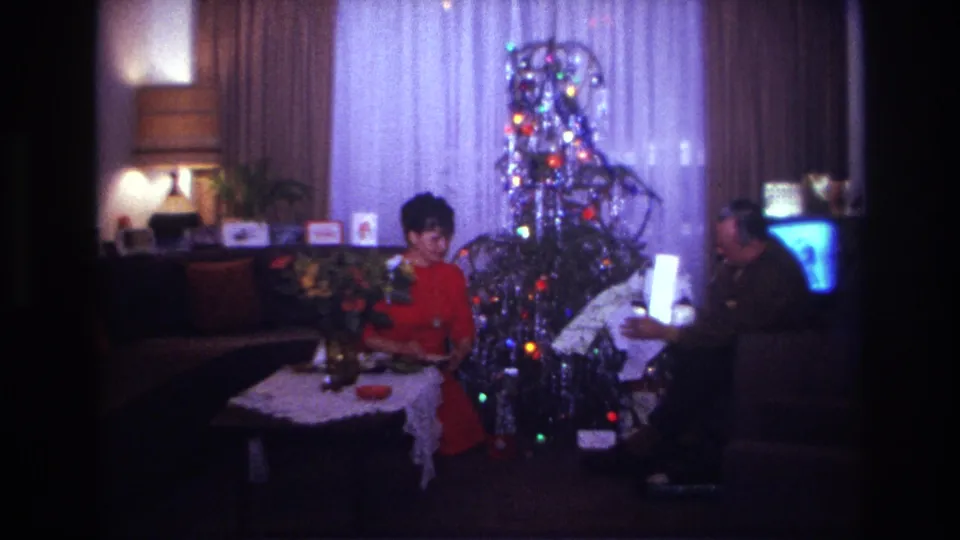 1967 Rockaway Beach holiday frame with a man holding a bright package and a woman seated beside a tinsel-covered Christmas tree.