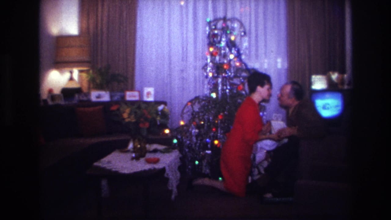 1967 Rockaway Beach home-movie frame of two adults kissing near a tinsel Christmas tree and glowing television.