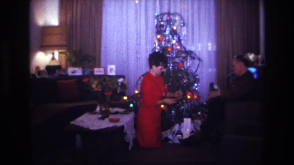 1967 Rockaway Beach home-movie frame with a woman and man beside a tinsel Christmas tree, gifts, table, lamp, and television.