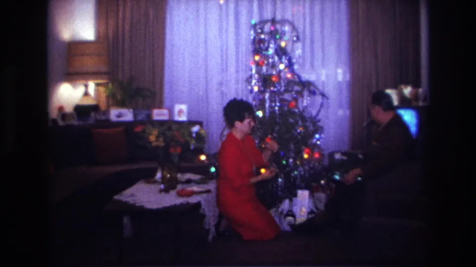 Rockaway Beach 1967 holiday frame with a woman adjusting the lit tinsel tree and a seated man partly in shadow.