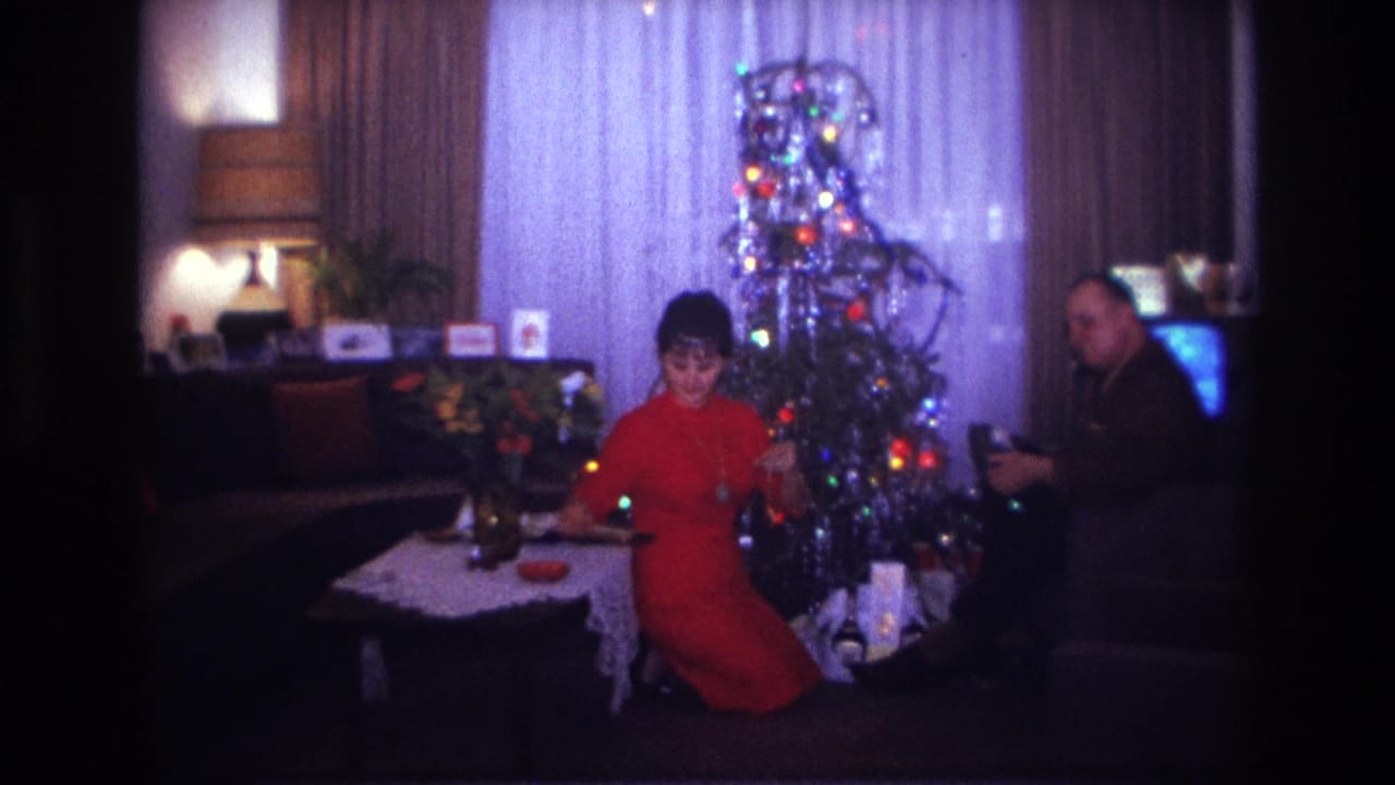 1967 Rockaway Beach living-room frame with a woman in red near the Christmas tree and a seated man beside gifts and a glowing television.