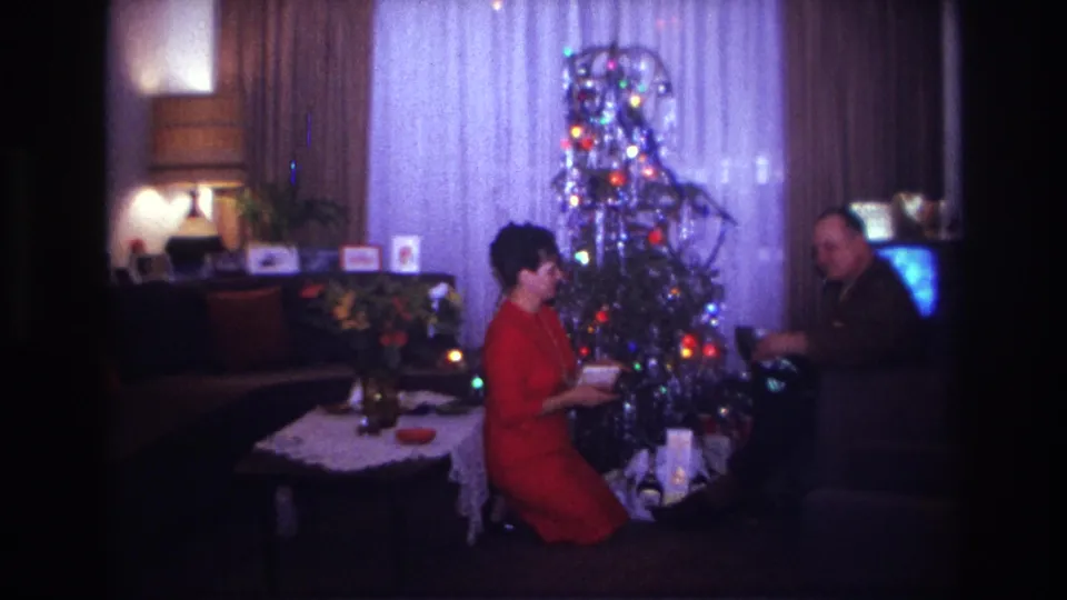 Rockaway Beach 1967 frame with two adults by a tinsel-covered Christmas tree, presents, drapes, and a television.