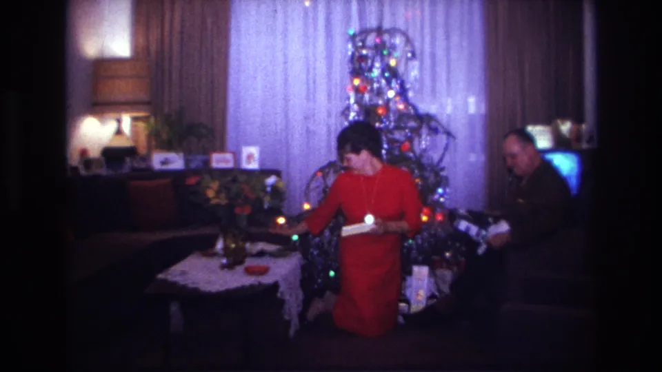 Rockaway Beach 1967 Christmas living-room frame with a woman kneeling, a man seated, tree lights, gifts, and a television.