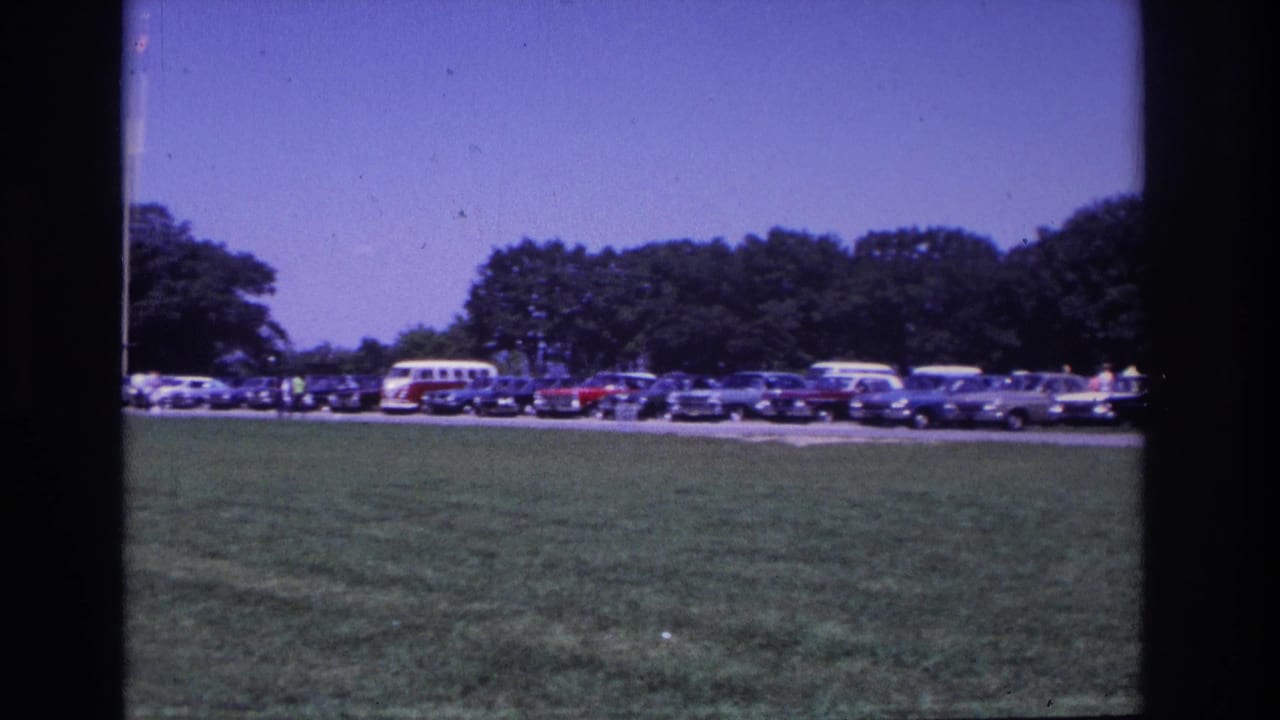 Ocean City, New Jersey 1968 frame showing a broad grassy parking area, rows of classic cars, a VW bus, visitors, trees, and a flagpole.