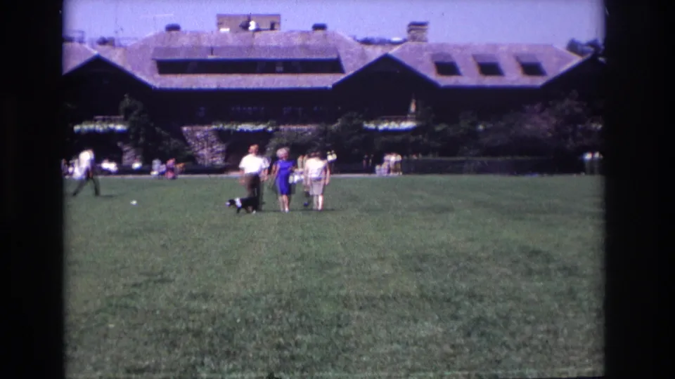 People walk a black and white dog across a broad Ocean City lawn in 1968, with a long dormered building in the background.