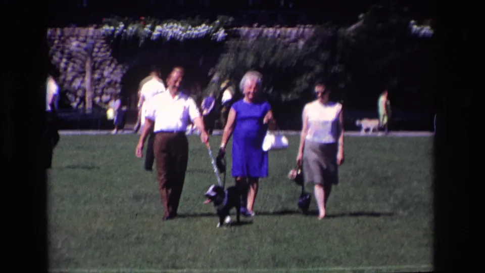 A man in a white shirt and two women walk toward the camera with a small leashed dog on a bright lawn in Ocean City, New Jersey.
