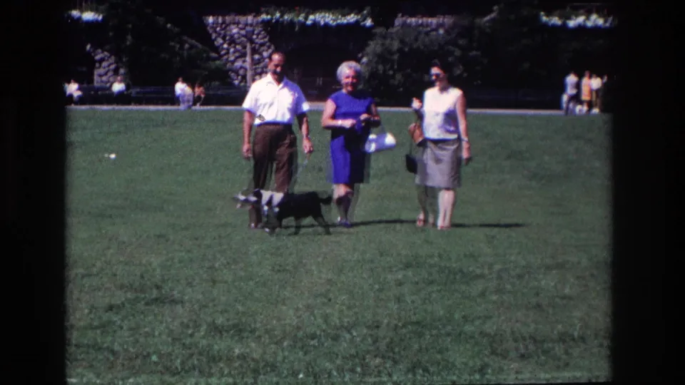 In the final frame, the man and two women continue across the Ocean City lawn with the small black-and-white dog walking near their feet.