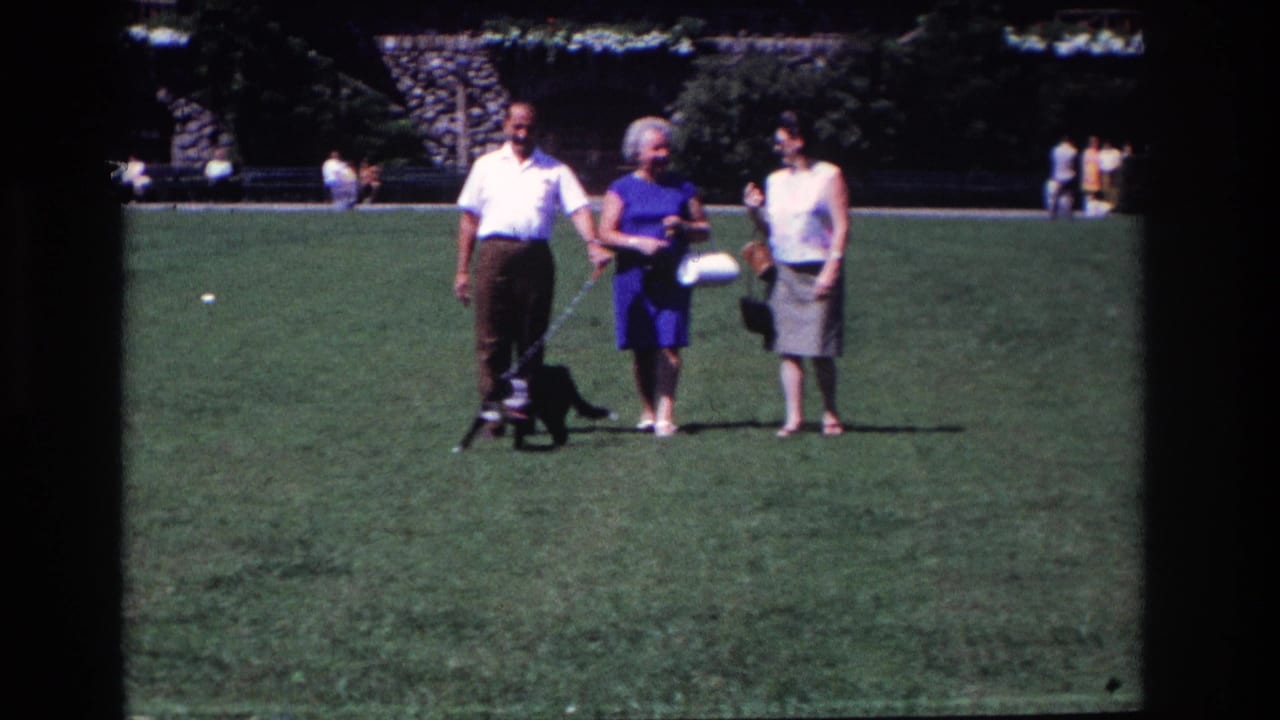 In 1968 Ocean City, New Jersey, three adults walk slowly across a grassy park with a small black dog on a leash.