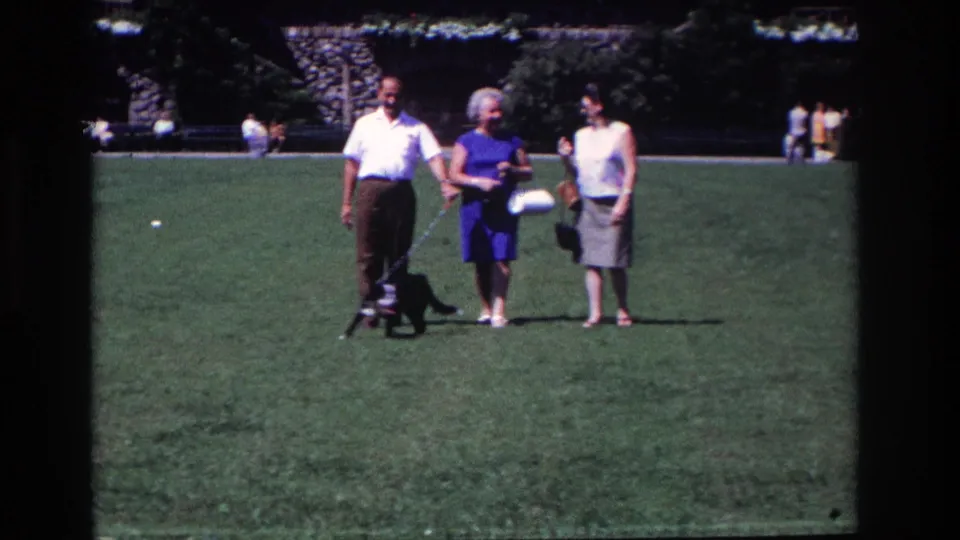 In 1968 Ocean City, New Jersey, three adults walk slowly across a grassy park with a small black dog on a leash.