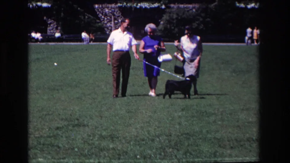 The group stands in a sunlit Ocean City park as the small black dog moves on its leash beside them.