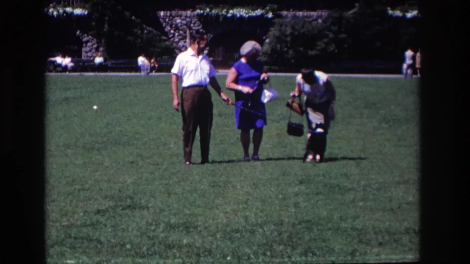 One woman bends toward the small dog while the man and another woman stand nearby in the 1968 park scene.