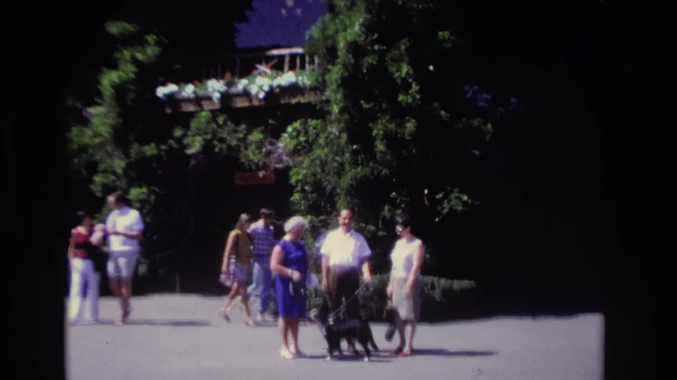 Adults in summer attire stroll near an ivy-covered Ocean City house in 1968, with a leashed black dog in the foreground.