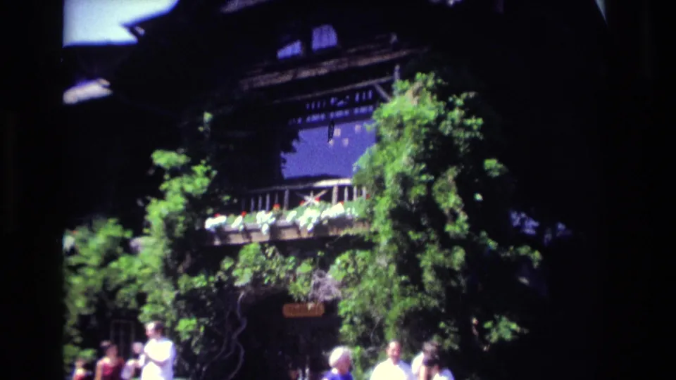A large Ocean City house with ivy, balcony railings, and flower boxes fills the frame as people pass below.