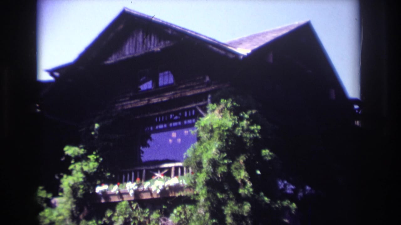 Dark wooden building with balcony and trees in bright sun.